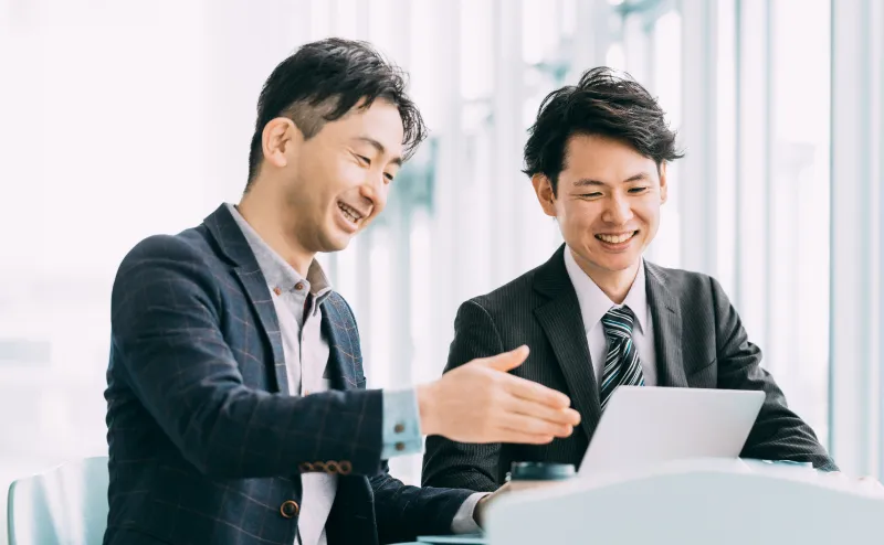 ノートパソコンを見ながら笑顔で話す二人の男性